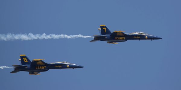 Two U.S. Navy Blue Angels jets flying in formation with smoke trails.
