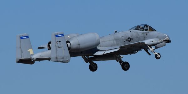A military A-10 Thunderbolt II jet in flight with landing gear down.