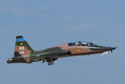 A military jet aircraft in flight against a clear blue sky.