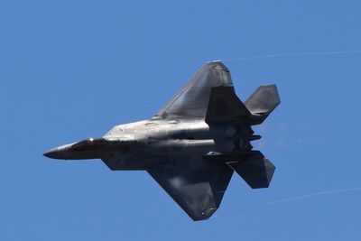 A fighter jet flies against a clear blue sky.