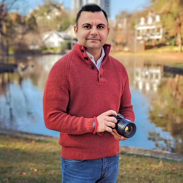 Man holding camera with a lake in the background. 