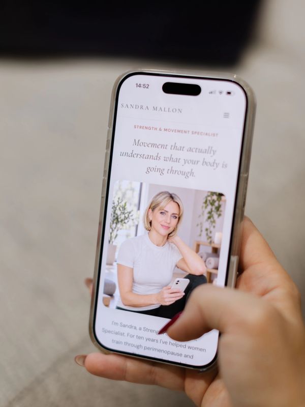 Woman holding phone displaying fitness website.