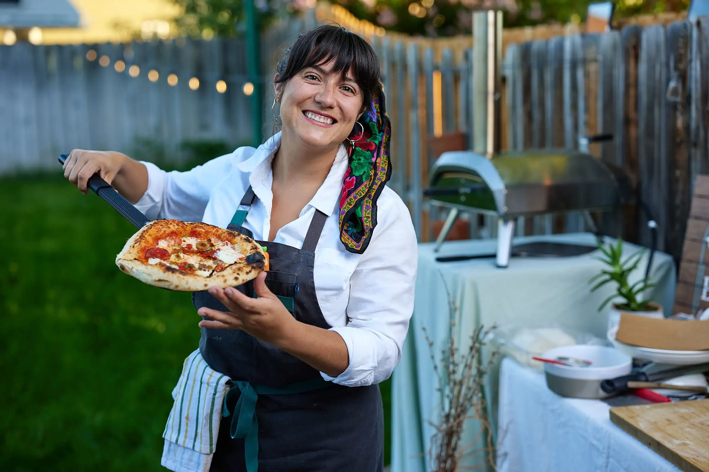 Smiling woman holding a freshly baked pizza outdoors.