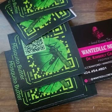 Mosquito Butter packets stacked with a business card on a wooden surface.