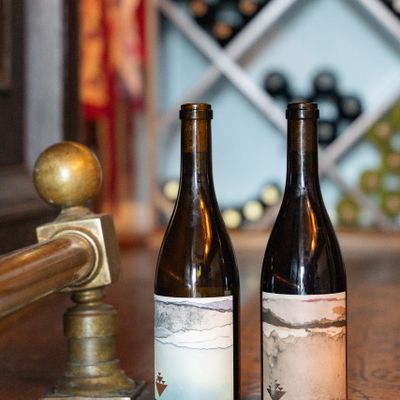 Two wine bottles on a wooden surface with a wine rack in the background.