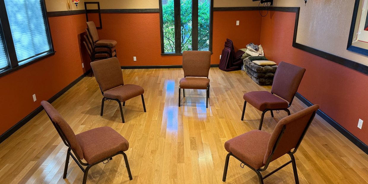 A circle of five brown chairs in a cozy room with wooden floors.