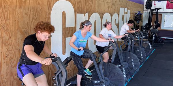 Four people exercising on stationary bikes at a CrossFit gym.