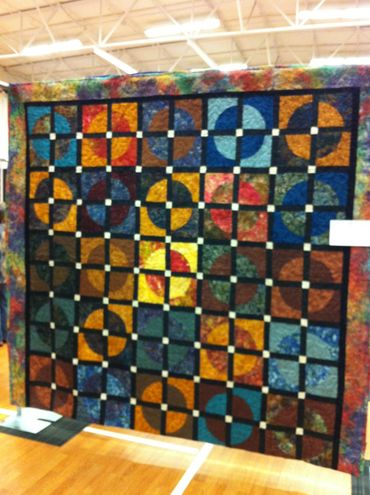 Colorful geometric quilt with circular patterns and square blocks.