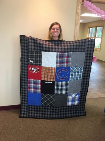 Woman proudly holding a handmade patchwork quilt with various fabric squares.