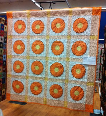 A quilt with orange and yellow flower patterns on a white background.