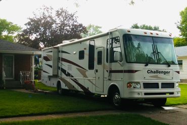 A large white Challenger RV parked on a lawn beside a house.