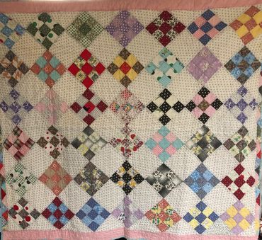 A colorful patchwork quilt with a pink border and various patterned squares.