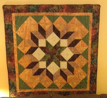 Colorful geometric patterned quilt hanging on a wall.