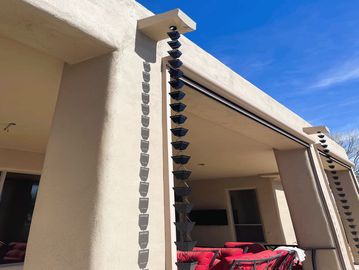 Modern rain chain hanging from a beige patio roof.