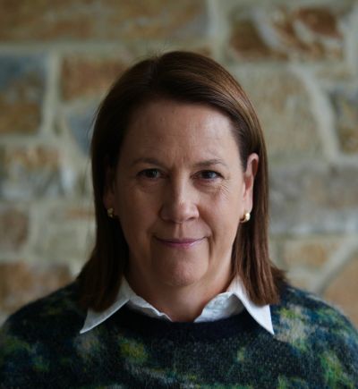 Portrait of a woman with brown hair in front of a stone wall.