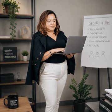 Mulher em escritório usando laptop, com quadro branco sobre gestão de RH ao fundo.