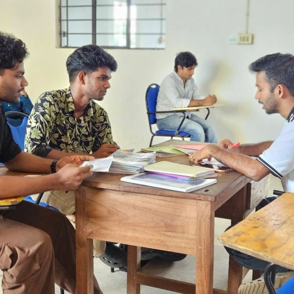 Young men engaged in a discussion around a table with books and papers.