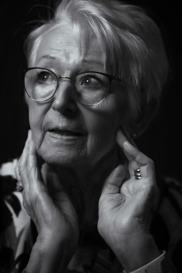 Black and white portrait of an elderly woman with glasses touching her face.