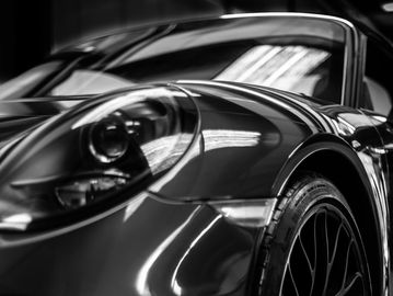 Black and white close-up of a sports car's headlight and wheel.