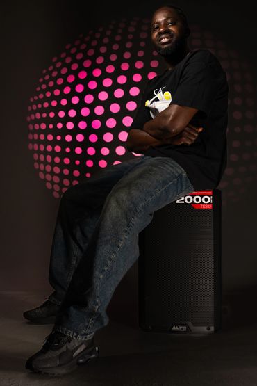 Man sitting on a speaker with a pink dotted light pattern behind him.