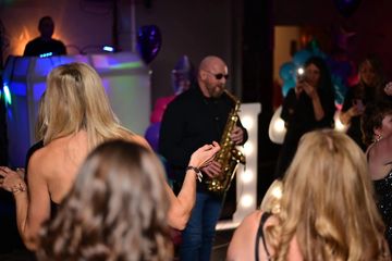 A saxophonist entertains a lively crowd at a colorful party.