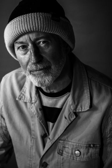 Black and white portrait of a thoughtful older man wearing a beanie and jacket.