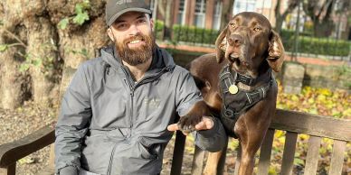 man smiling whilst sitting on park bench with dog 