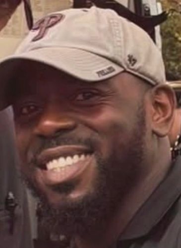 Smiling man wearing a beige baseball cap.