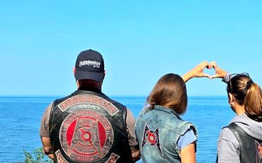 Four bikers by the sea, two forming a heart with their hands.