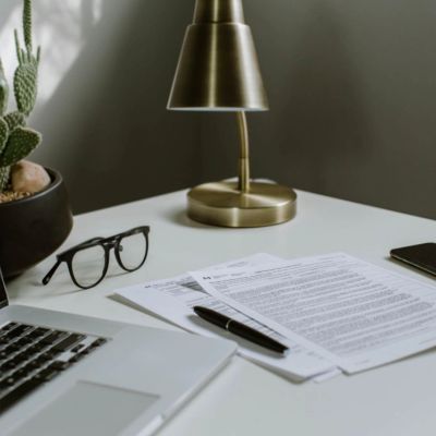 Workspace with laptop, glasses, documents, and lamp.