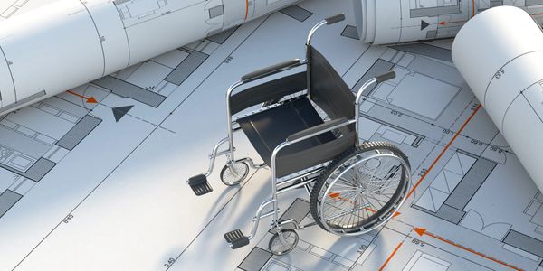 Wheelchair placed on architectural blueprints with rolled plans around.