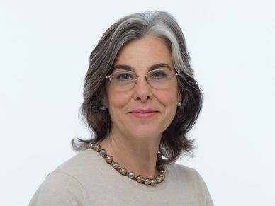 Confident middle-aged woman with glasses and pearl necklace smiles gently.
