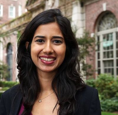 Black and white portrait of a smiling woman outdoors in front of a historic building.