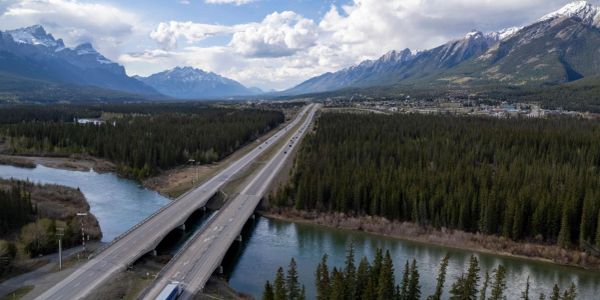 Highway crossing a forested area with mountains in the background.
