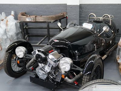 A black unregistered Morgan 3 wheeler car waits patiently against the factory wall at Morgan Malvern