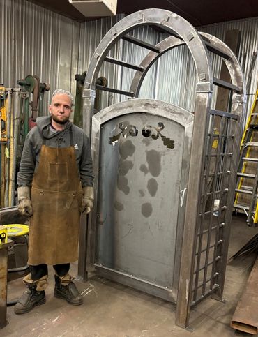 Man in workshop standing beside a large metal door frame.