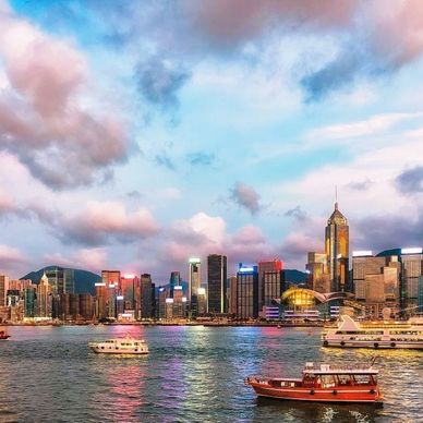 Colorful city skyline at sunset with boats on the water.