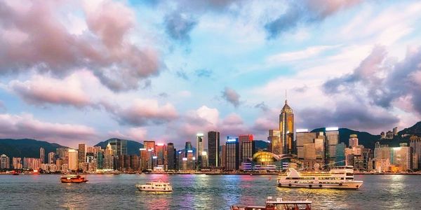 Vibrant city skyline with boats on water under a colorful sky.