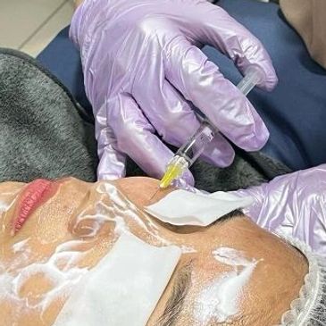 A woman receives a facial injection from a masked professional in a clinic.