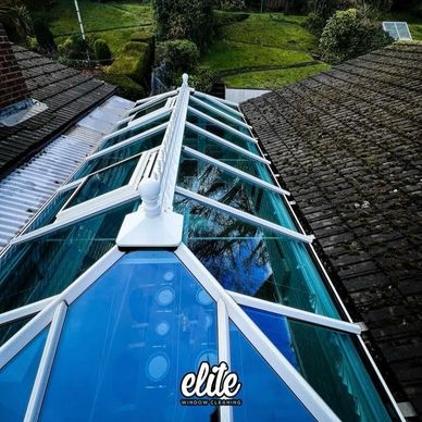 Clean glass roof reflecting clear skies over a garden area.
