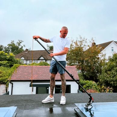 Man cleaning a rooftop window with a long brush.