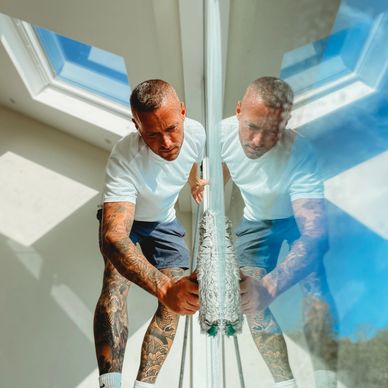 Man cleaning a glass window with a mop, reflection visible.
