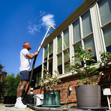 Man cleaning high windows with a long vacuum hose on a sunny day.