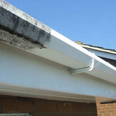 A white gutter attached to a house roof against a clear blue sky.