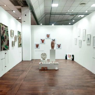 Art gallery with sculptures and paintings displayed on white walls and wooden floor.