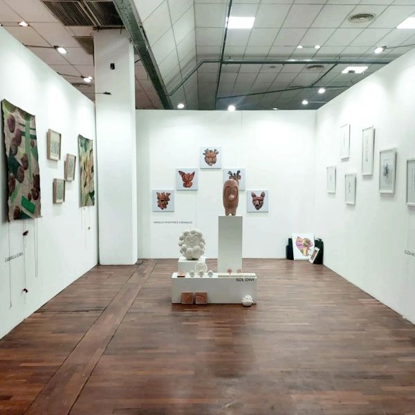 Art gallery with sculptures and paintings displayed on white walls and wooden floor.