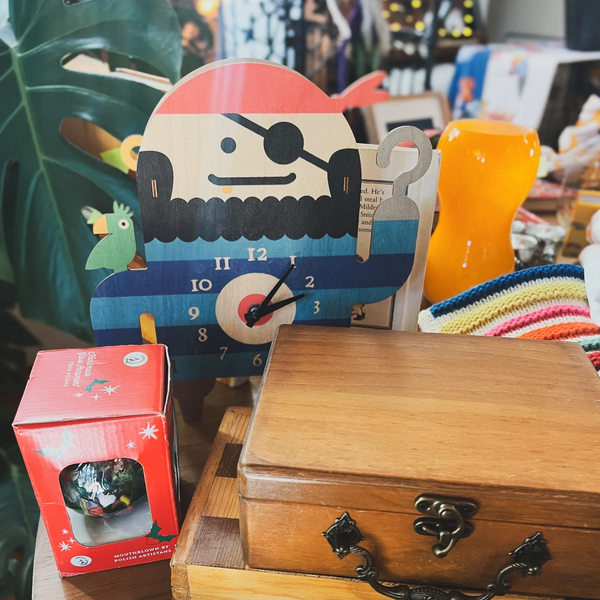 Colorful pirate-themed clock with wooden boxes and a red ornament on a table.