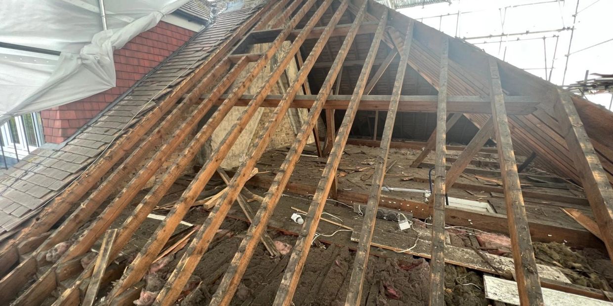 Roof under construction exposing wooden beams and insulation.