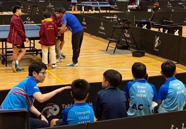 Coach instructing young table tennis players during practice.