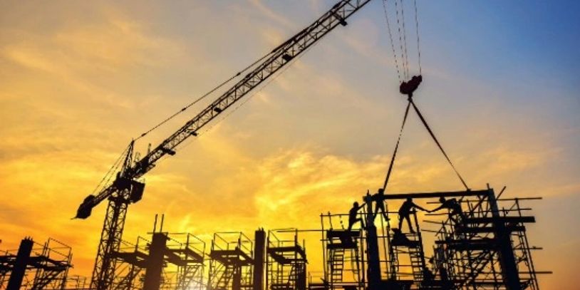 Construction workers and crane at sunset on a building site.